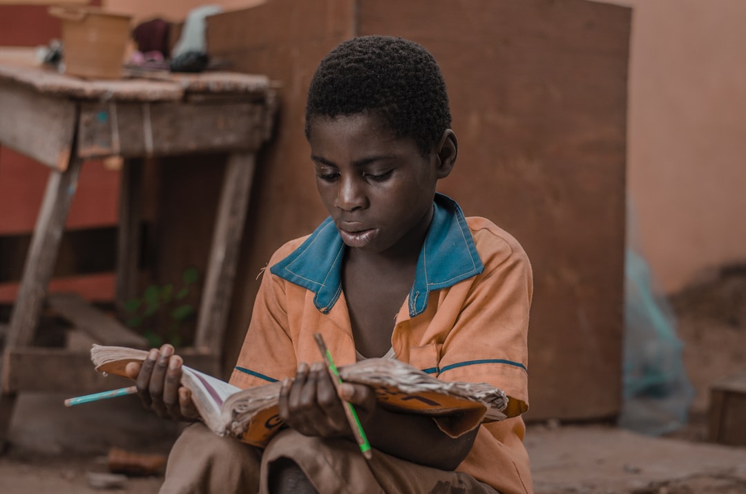 “Young African village boy sitting outside his home, reading an old, worn-out book”