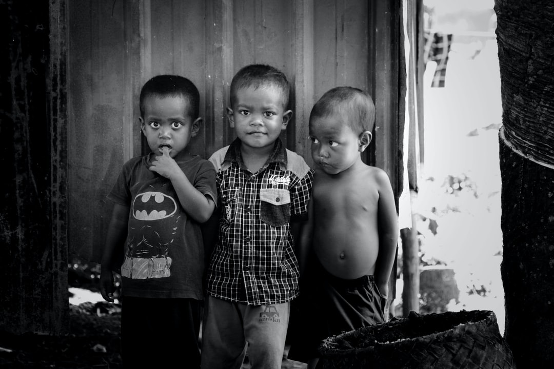 “Three African children sitting in a line, tired and hungry, with thumbs in their mouths”